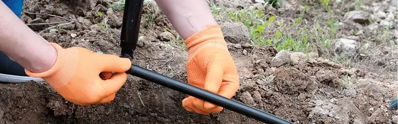 A person digs in the dirt using a pipe, demonstrating a manual excavation technique.