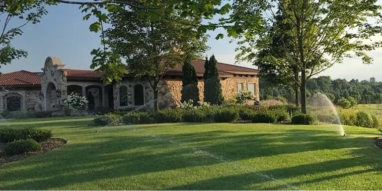 A large house surrounded by a well-maintained lawn with sprinklers watering the grass.