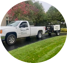 A white truck towing a trailer, parked on a road with trees in the background.